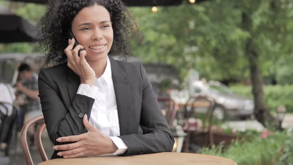 African Woman Talking on Phone Sitting in Outdoor Cafe