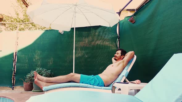 Joyful Young Man is Relaxing and Sunbathing on Lounge Chair with Hands Behind Head