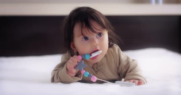 Baby Lies on Her Stomach on the Bed in the Nursery and Licks the Nipple Holder