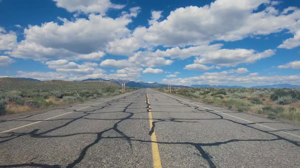 Small Asphalt Road Surrounded By Desert with Clouded Blue Sky.