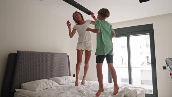 Happy Mom Have Fun Jumping with Little Son on Bed