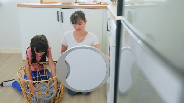 Young little cute girl child help and learn from parent mom to put laundry in washer appliance.