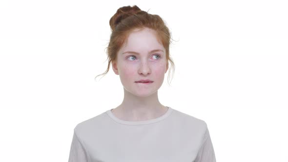 Caucasian Thoughtful Young Woman with Tied Ginger Hair in Topknot Looking From Side to Side Biting
