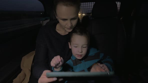 Mother and son playing with touch pad during night car ride