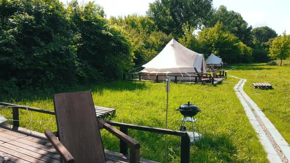 Glamping tents with chairs in the nature, green grass and trees, trail