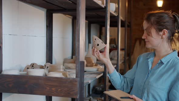 Slow Motion of Young Woman Looking at Hand-made Earthware Then Taking Notes in Workshop