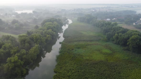 Foggy Morning Over a Plain and River Floodplain Meadow Near a Rural Village with a House