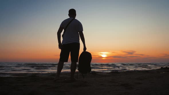 Silhouette of Traveler Man with Backpack Enjoys Sunset on Tropical Sea Beach. Traveling Along Coast