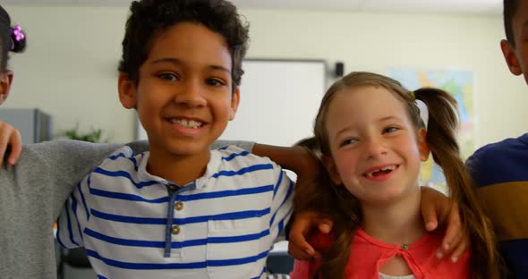 Front view of happy multi-ethnic schoolkids with arm around standing in classroom at school 4k