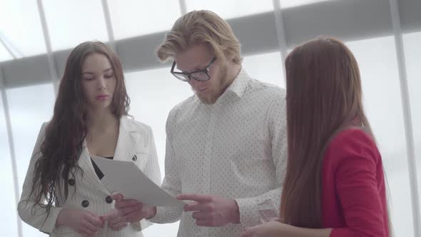 Blond Man in Glasses Explaining His Idea To Two Female Colleagues Standing on Either Side of Him in