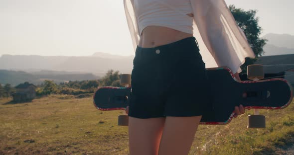 Attractive Stylish Woman Walk on Country Road Holding Longboard Skate at Sunset