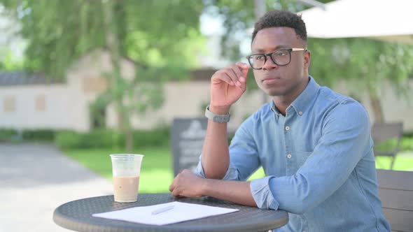 Pensive African Man with Coffee and Documents Thinking in Outdoor Cafe