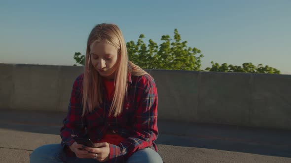 Portrait of Woman Skater on Skateboard Networking on Phone at Sunrise