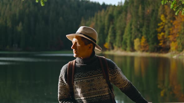 Traveler Hipster Man in Hat Standing on Pier and Admiring Mountain Lake Among Forest