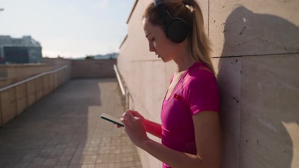 Sportswoman is Using Mobile App with Music for Workout Standing in City Street After Training