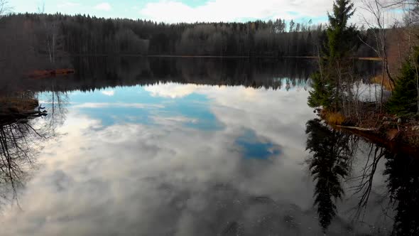 Flying at low altitude over a small lake with green trees, a yellow field and the blue sky with the