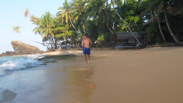 Sporty Muscular Man in Blue Shorts Runs Along Coastline