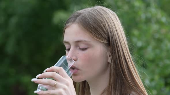 Portrait of a young girl who drinks mineral water from a glass in nature