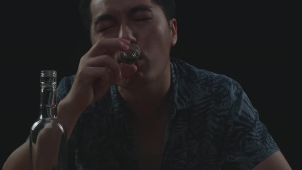 Close Up Of Drunk Asian Man Cheering Vodka Glass To Camera Before Drinking In Black Background