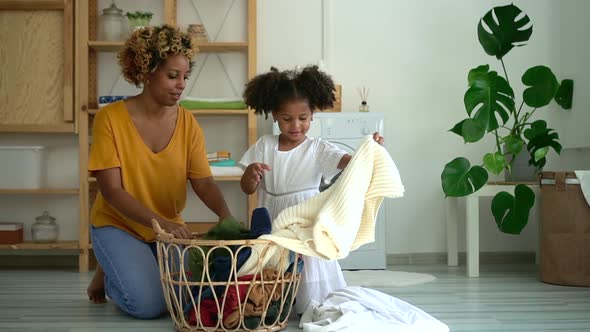 Young Mother and Daughter Lay Out Clothes While Sitting on Floor in Laundry at Home Spbd