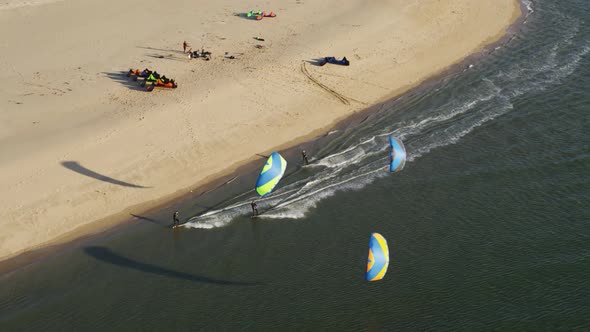 Three kitesurfers glide on the ocean water along a sandy beach shore in an aerial drone shot.