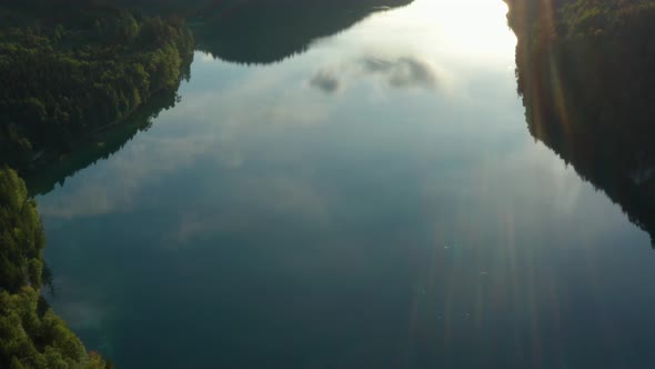 Aerial pan up, Alpsee reflection of mountains and clouds, lens flare