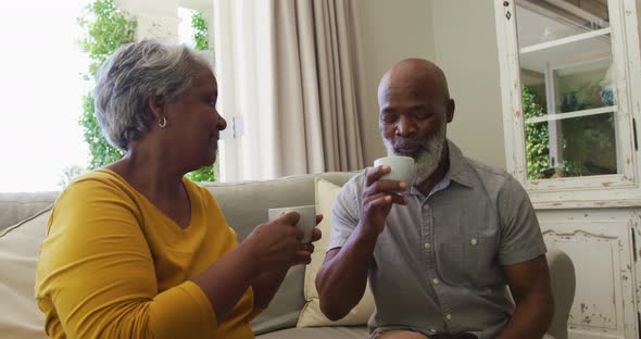 African american senior couple smiling while having coffee together sitting on the couch at home