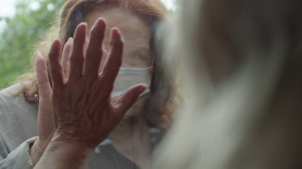 a Woman Visits Her Elderly Mother Putting Her Hand to the Glass and Showing Support During the