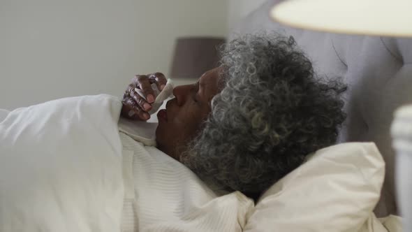 Sick senior african american woman coughing while lying on the bed at home