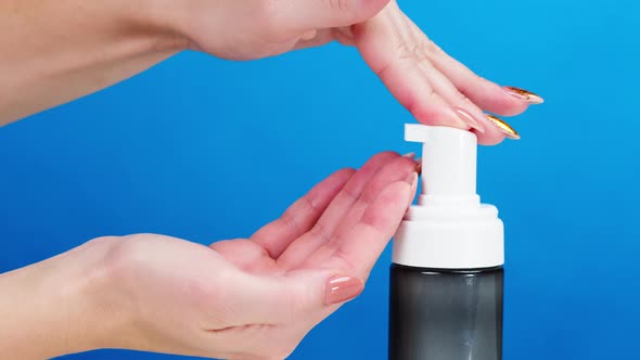 Female Hands Pushing Dispenser and Using Liquid Soap on Blue Background