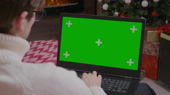 Over the Shoulder: Man Using Laptop with Mock-up Green Screen.