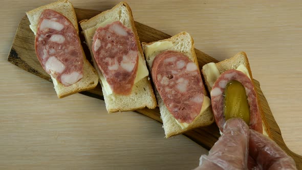 Human Hand Puts Sliced Pickled Cucumber on Sausage Sandwiches.