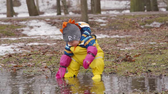 Cute Child in Yellow Waterproof Rain Pants Bibs for Kids and Rubber Boots on a Walk in Park in Early