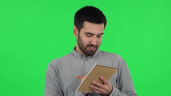 Portrait of Brunette Guy Is Thinking, Then Writing with Pencil in Notebook. Green Screen