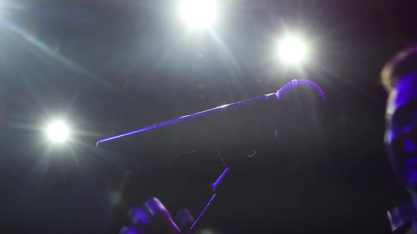 Man Testing Microphone on Stage in Spotlight in Dark Preparing To Performance.