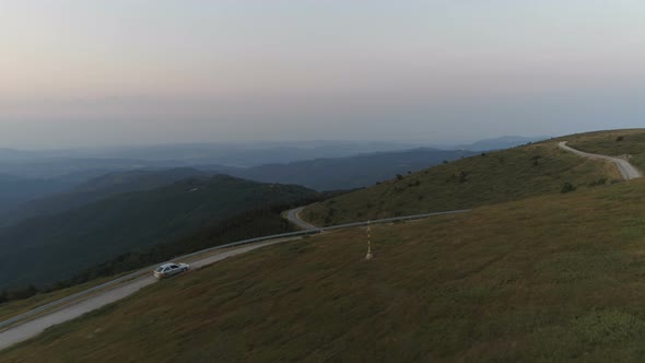 Drone Follows Car Driving Down a Mountain Pass Road with Deep Valley Background