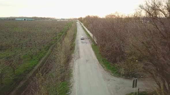 the Car Drives Along the Village Road Along Agricultural Buildings and Gardens