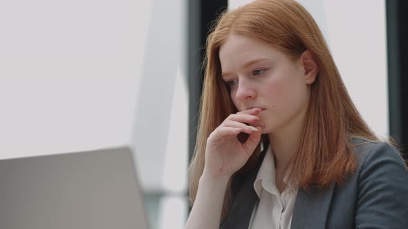 Thoughtful Concerned Redheaded Woman Working on Laptop Computer Looking Away Thinking Solving