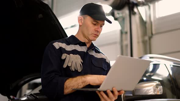 Car Mechanic Working on Laptop in Auto Repair Service Lean on a Car Low Angle View