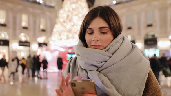 Portrait of young beautiful brunette woman in winter jacket and scarf typing message on mobile phone