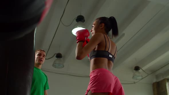 Sporty Fit Black Female Boxer with Trainer Training Punching Heavy Bag Indoors