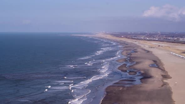 Rough waves break on empty Scheveningen beach with Den Haag backdrop - aerial