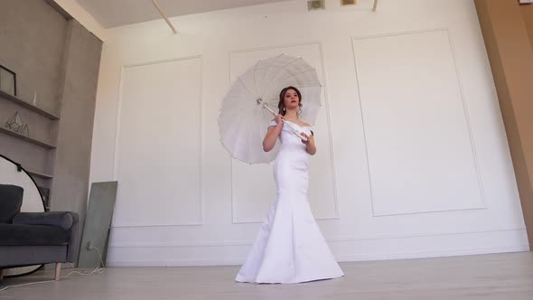 Beautiful Girl in a Wedding Dress Posing with a White Umbrella on Her Shoulder