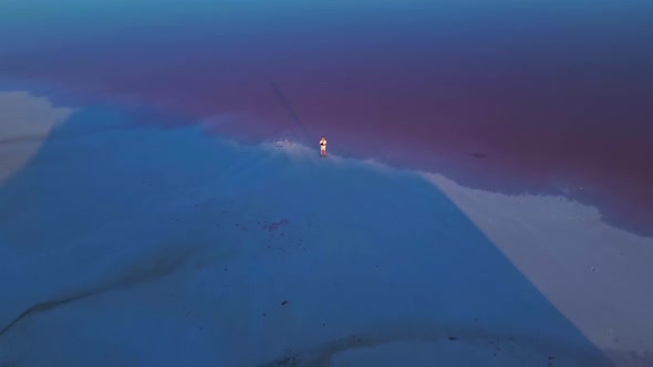 Drone Flying From Man Pilot Standing on Coast of Pink Lake at Sunset