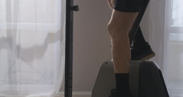 Man on Exercise Bicycle Training at Home Closeup View of Feet on Pedals Tensing Muscles of Legs