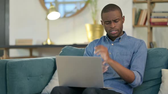 Young African Man with Laptop Having Wrist Pain on Sofa