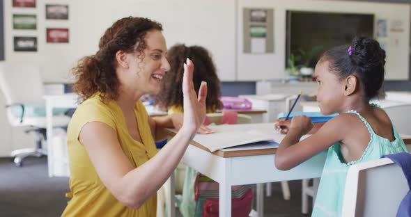 Video of happy caucasian female teacher clapping hands with african american girl during lessons alt
