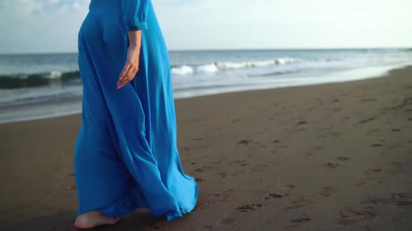 Woman in Beautiful Blue Dress Walking Along a Black Volcanic Beach