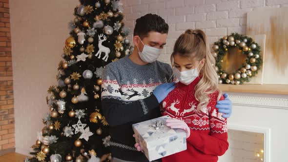 Man Hugging His Girlfriend Give Gift on Xmas Wearing Medical Masks and Gloves