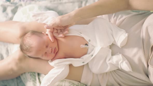 newborn baby top view lies on her lap mother caresses the child's hand alt